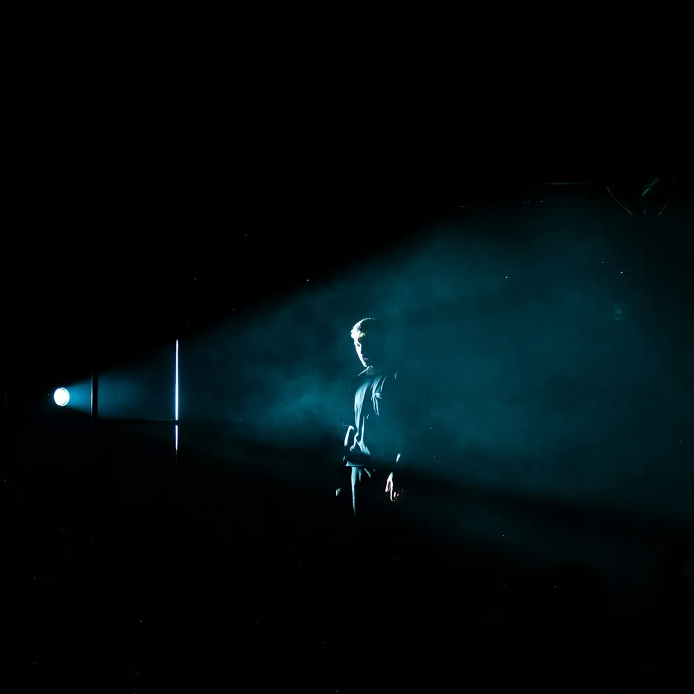 A lone figure standing in a single beam of light on a darkened stage